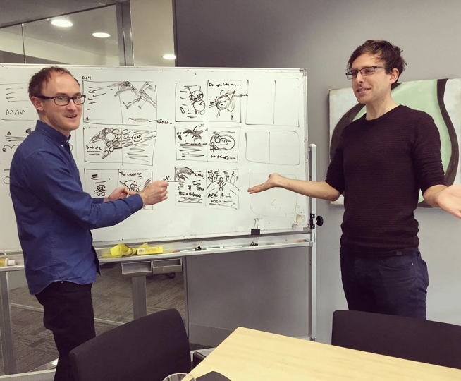 Ben Wood and Andrew McDonald sketching out pages of Real Pigeons Fight Crime together on a whiteboard