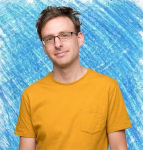Photo of author Andrew McDonald, wearing a yellow t-shirt. The background has been coloured blue by a blue crayon.